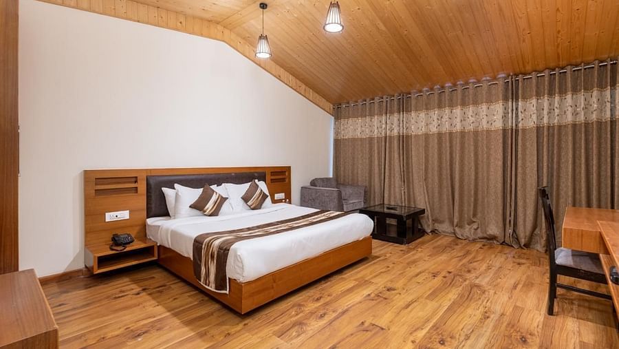This photo captures a cosy and inviting hotel room with a warm wood-panelled ceiling and large windows that bring in plenty of natural light  | DLS Serenity Resort and Spa